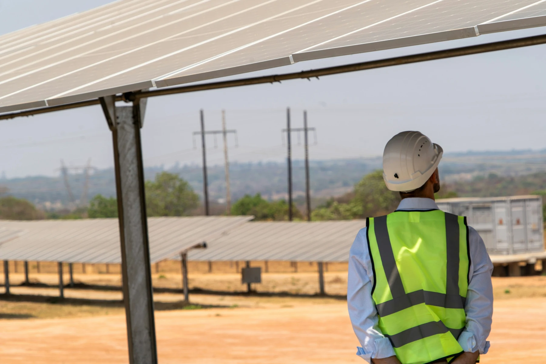 Inspection d'une installation solaire rurale Technicien casqué observant une grande installation photovoltaïque au sol